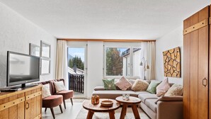 Una sala de estar moderna con televisor de pantalla plana, muebles de madera, un sofá y vistas al exterior.