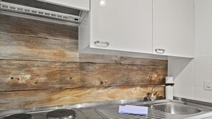 Cocina con estufa de acero inoxidable, un lavamanos y paneles de madera en las paredes.