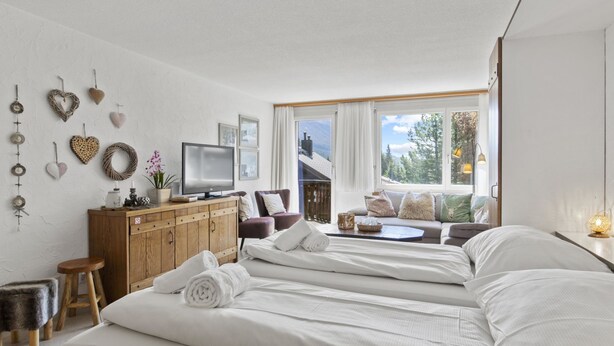Una habitación de hotel moderna con una cama grande, un aparador de madera, un televisor y vistas al exterior.