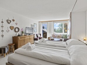 A modern hotel room with a large bed, a wooden dresser, a television, and a view of the outdoors. - Apartment A302 by Interhome (Lenzerheide)