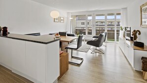 A modern kitchen with a central island, dining area with chairs, and a view of the city through large windows. - Nr.78 Haus Ladina by Interhome (Lenzerheide)
