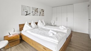 A modern bedroom with a wooden bed, white bedding, a nightstand, a chair, and a wardrobe. - Nr.78 Haus Ladina by Interhome (Lenzerheide)