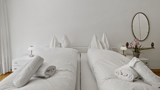 A hotel room with two beds, white linens, a bedside table with a lamp, a mirror, and a small potted plant. - Nr.58 Haus Ladina by Interhome (Lenzerheide)