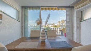 Een eethoek met een houten tafel, twee stoelen, een vaas en uitzicht op een balkon met een balustrade en een gebouw op de achtergrond.