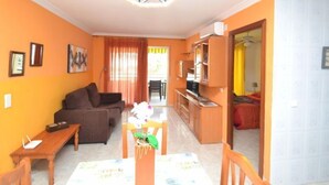 Een woonkamer met een bank, een eettafel met stoelen, en een keuken met een koelkast en kasten.