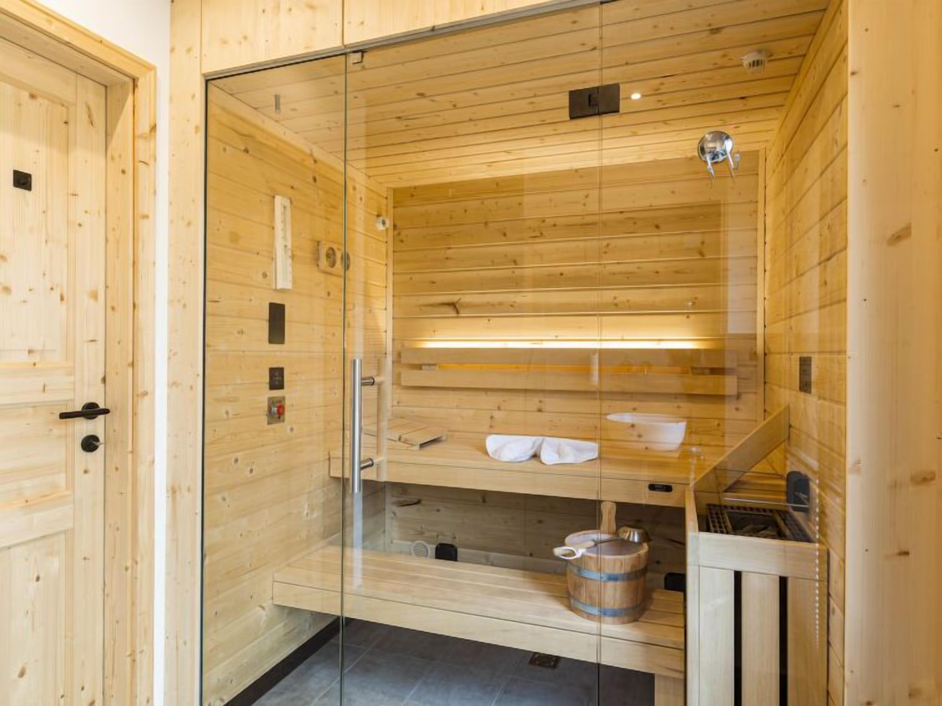Een houten sauna met glazen wanden, een bank, een emmer en een handdoekhouder.