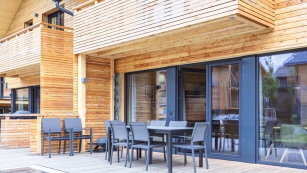 A wooden deck with a pool, outdoor seating, and a glass door leading to a covered area. - #5b mit Sauna & Pool by Interhome (Sankt Georgen am Kreischberg)