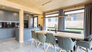 A modern kitchen with grey cabinets and a wooden ceiling, a dining area with grey chairs and a wooden table, and large windows with curtains. - #5b mit Sauna & Pool by Interhome (Sankt Georgen am Kreischberg)