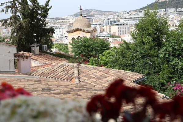 Un terrat amb teules de terracota, envoltat de vegetació i un paisatge urbà al fons.