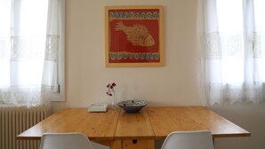 A dining area with a wooden table, white chairs, a vase with flowers, and a framed picture on the wall. - In the shadow of Acropolis - Breathtaking view  (ATHENS)
