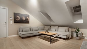 A modern loft bedroom with a sloped ceiling, a large window, a sofa bed, a coffee table, and a painting of moons. - ARCTIC HOMES - THE RETREAT (Tromsø)