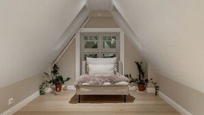 A narrow, high-ceilinged room with a bed centered under a window, flanked by potted plants. - ARCTIC HOMES - THE RETREAT (Tromsø)