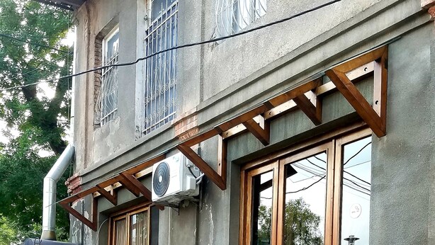 Um edifício com varanda de madeira, plantas em vasos e um grande aparelho de ar condicionado.
