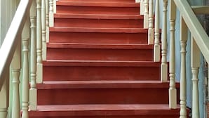 Uma escadaria com degraus vermelhos e balaústres brancos que leva a uma porta.