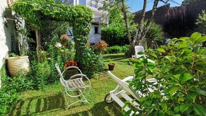 A well-maintained garden with a white metal chair and a white lounge chair, surrounded by lush greenery and flowering plants. - Biarritz St Charles. Quiet garden, Walking distance to beaches and golf course (Biarritz)
