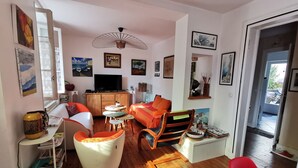 A cozy living room with a wooden floor, a television, and various artworks on the walls. - Biarritz St Charles. Quiet garden, Walking distance to beaches and golf course (Biarritz)