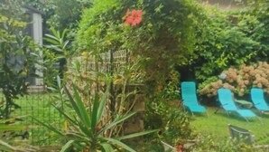 A garden with various plants and a small fence. There are also some blue chairs and a building with a red roof in the background. - Biarritz St Charles. Quiet garden, Walking distance to beaches and golf course (Biarritz)