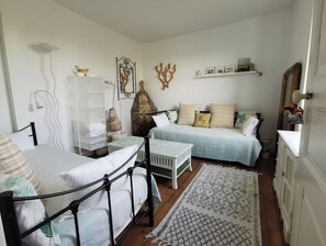 Un dormitorio con dos camas, un armario blanco, un espejo y una estantería con fotografías.