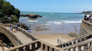 Un paseo marítimo con un puente de piedra que conduce a una playa de arena.