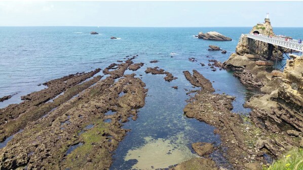 Paisagem costeira com formações rochosas e uma ponte que leva a um penhasco com um farol.