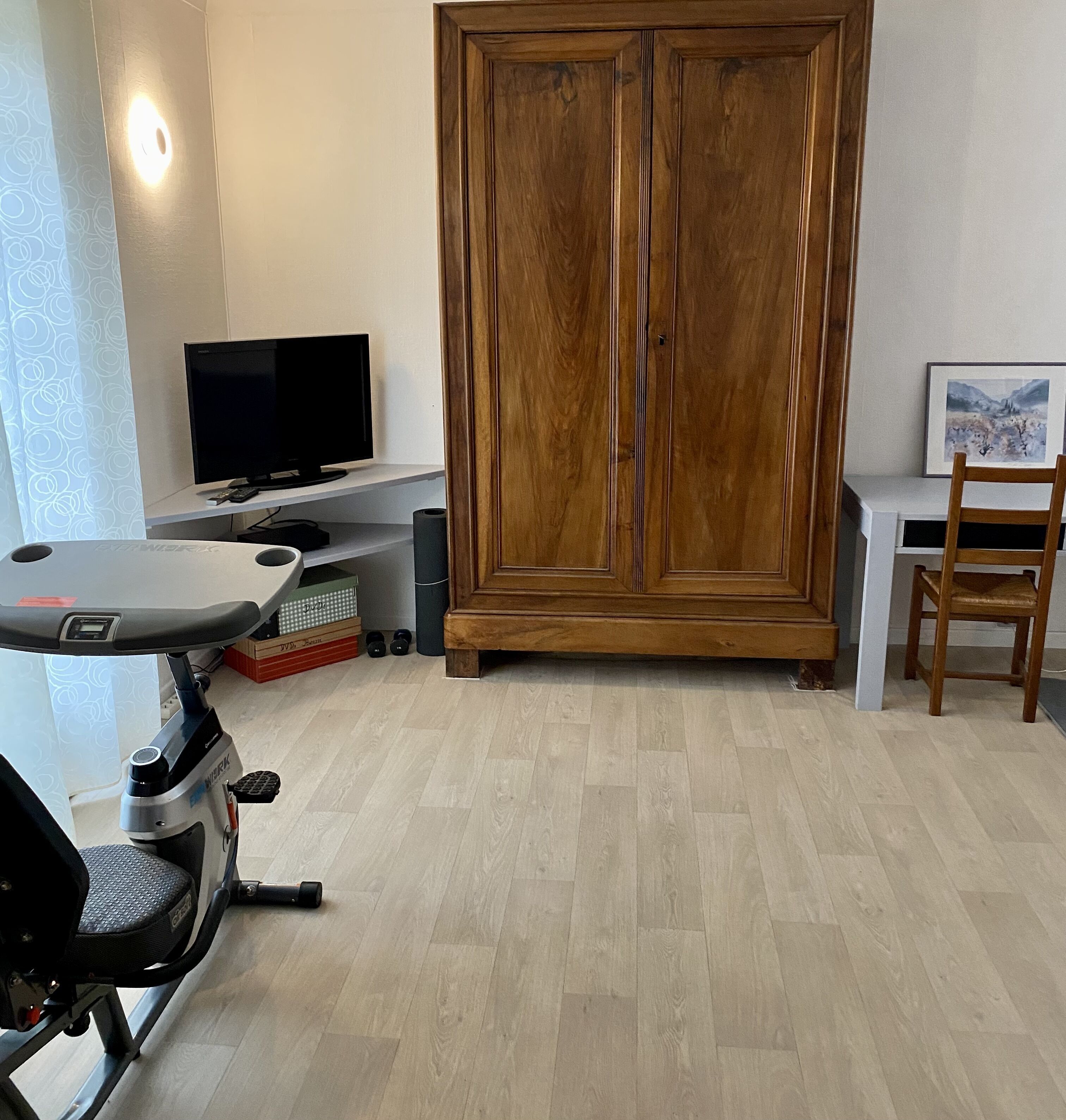 Ein Zimmer mit Holzschrank, Laufband, Fernseher und Schreibtisch mit Stuhl.