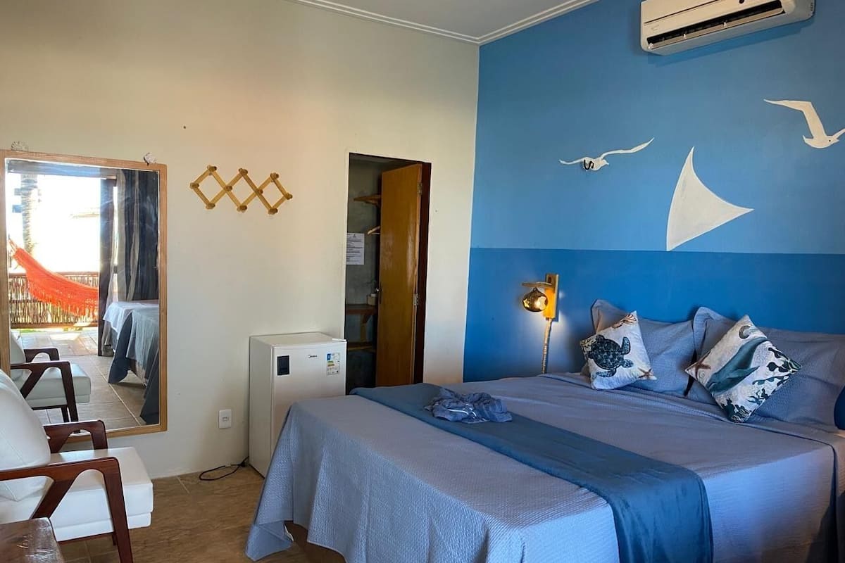 Ein Schlafzimmer mit einem Bett, einem Schreibtisch, einem Stuhl, einem Spiegel und einer Wand mit einem Meeresblick-Wandgemälde.