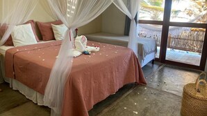 Una habitación con una cama cubierta de pétalos de rosa, un dosel y vistas a un espacio tropical al aire libre.