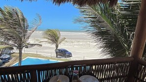 Un área de comedor frente a la playa, con vistas al océano, una piscina y palmeras.