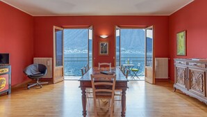 Comedor con mesa y sillas, un radiador, televisor y vistas a través de puertas abiertas.