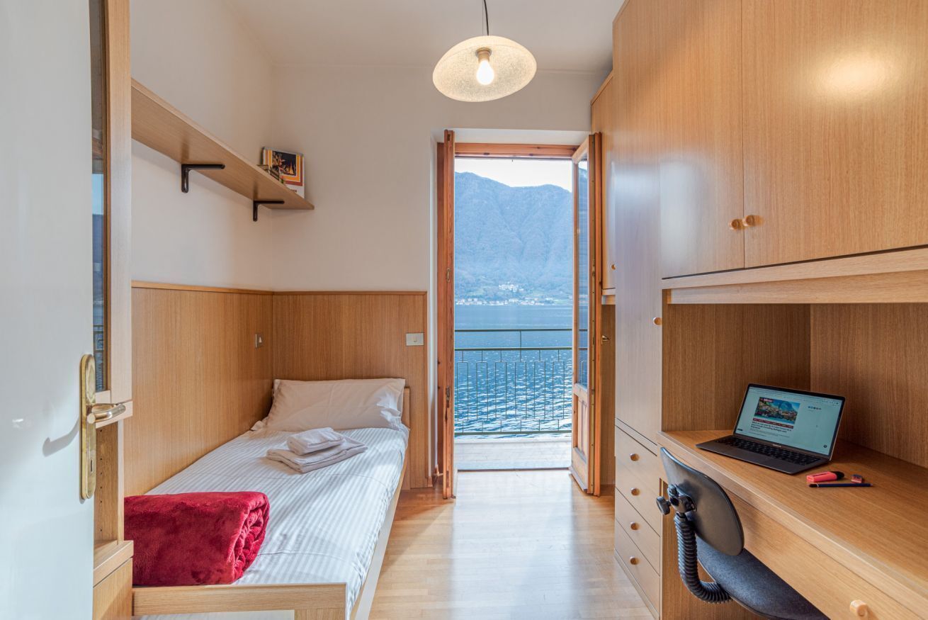 A compact room with a bed, a desk with a laptop, a telephone, and a view of the sea.