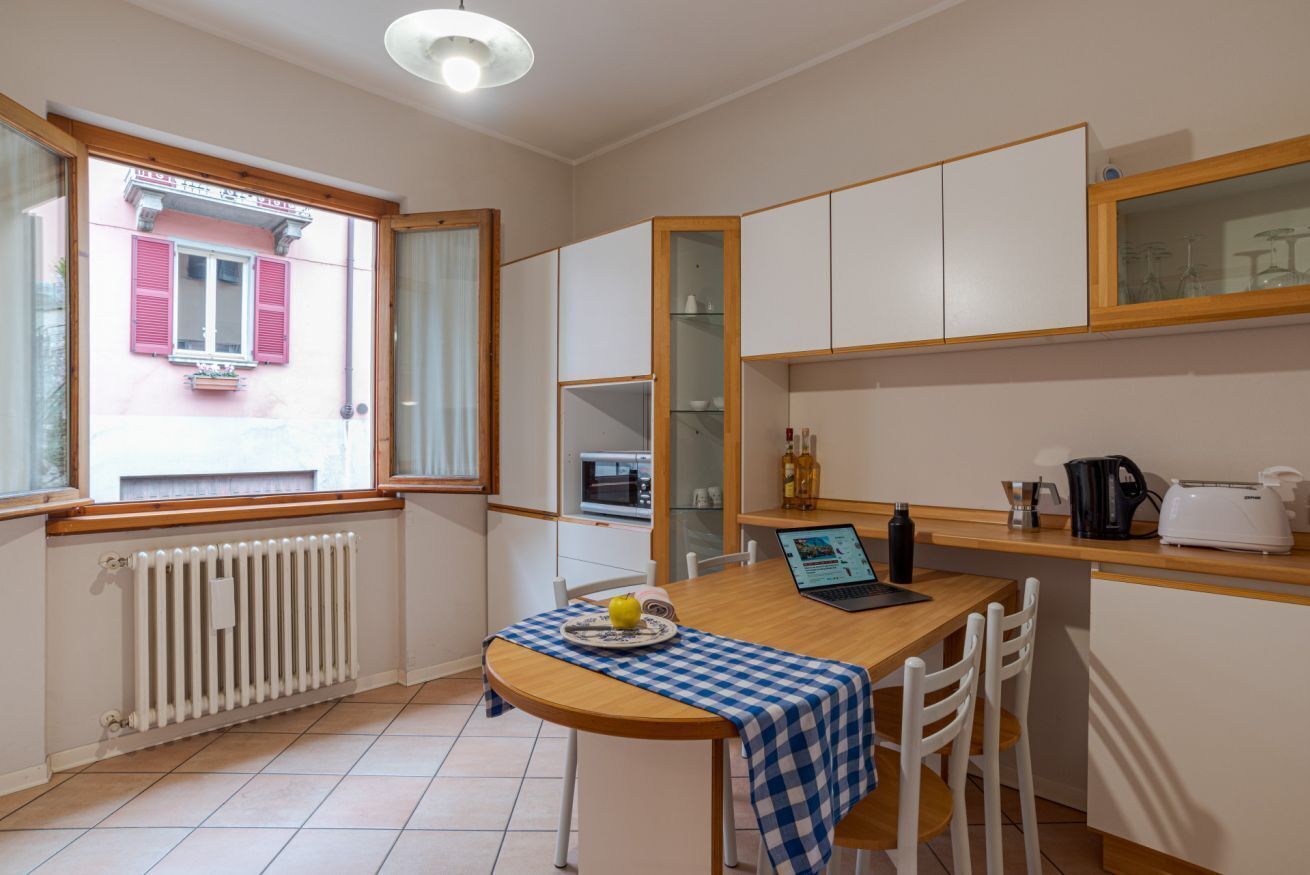 A compact kitchen with a dining area, a window with shutters, a built-in oven, and a refrigerator.