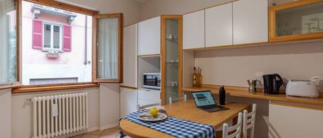 A compact kitchen with a dining area, a window with shutters, a built-in oven, and a refrigerator.