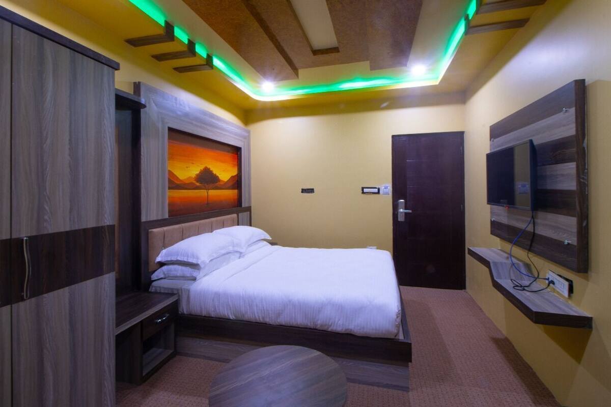 Une chambre à coucher avec un lit, une table de chevet, un téléviseur fixé au mur et un tableau accroché au mur.