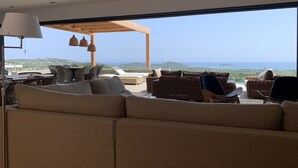 A modern outdoor seating area with a sofa, chairs, and a dining table, overlooking a scenic view of the sea and hills. - porto vechio saint cyprien (zonza)