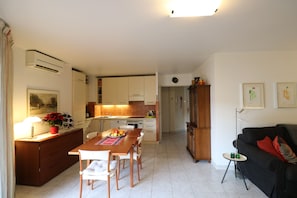 A modern kitchen with white cabinets, a dining table with chairs, and a black sofa in the living area.