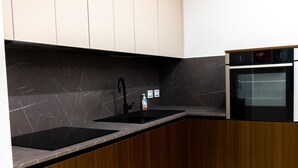 A modern kitchen with dark wood cabinets, a black countertop, a sink, and a built-in oven. - Jewel at Porta Nolana (Napoli)
