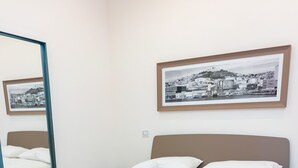 A neatly made bed with a fluffy blanket, a large mirror, and a framed cityscape picture on the wall. - Jewel at Porta Nolana (Napoli)