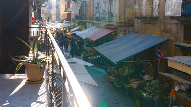 A narrow street with market stalls, stone buildings, and a balcony with a potted plant. - Jewel at Porta Nolana (Napoli)