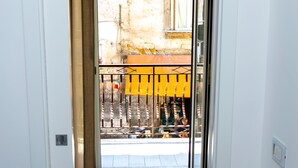 A hallway with a view of a balcony with yellow railings and a white door leading to an outdoor area. - Jewel at Porta Nolana (Napoli)