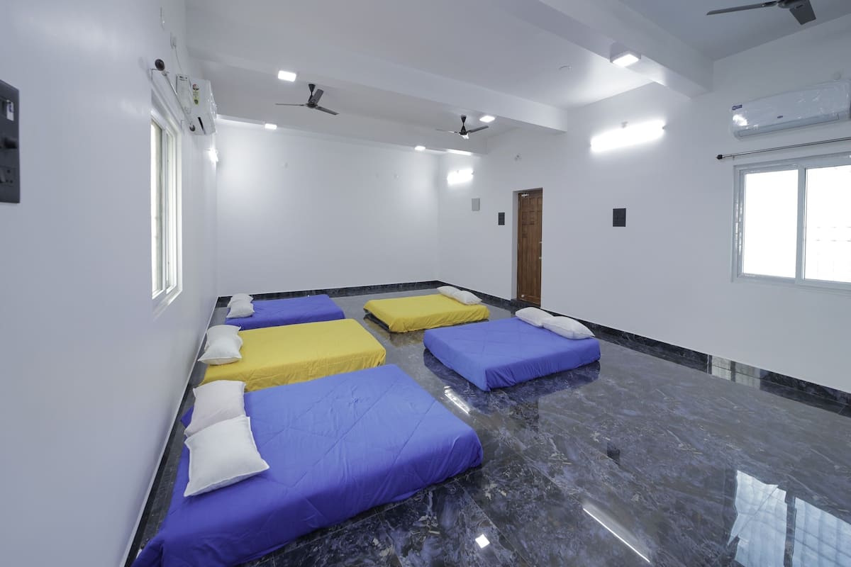 Quarto com quatro camas alinhadas, um ventilador de teto e janela com vista.