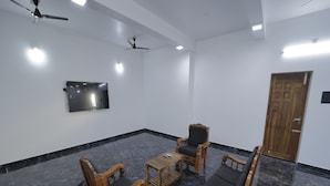 A room with a marble floor, wooden furniture, a ceiling fan, a flat-screen TV, and a wooden door. - APK Farm House (Noida)