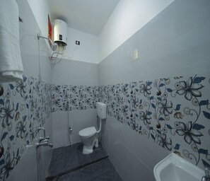 A bathroom with a toilet, shower, and bathtub. The walls are tiled with a floral pattern. - APK Farm House (Noida)