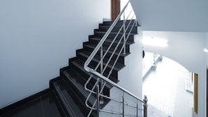 A modern staircase with black steps and metal railings, leading to a wooden door at the top. - APK Farm House (Noida)