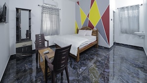 A bedroom with a bed, a desk, a chair, a ceiling fan, a mirror, a shower curtain, and a bathroom sink. - APK Farm House (Noida)