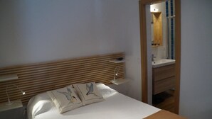 A bedroom with a wooden headboard, a bedside table with a lamp, a bed with two pillows, and a bathroom visible through an open door.
