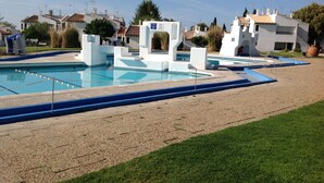 A swimming pool with a blue deck, surrounded by white structures and a grassy area.