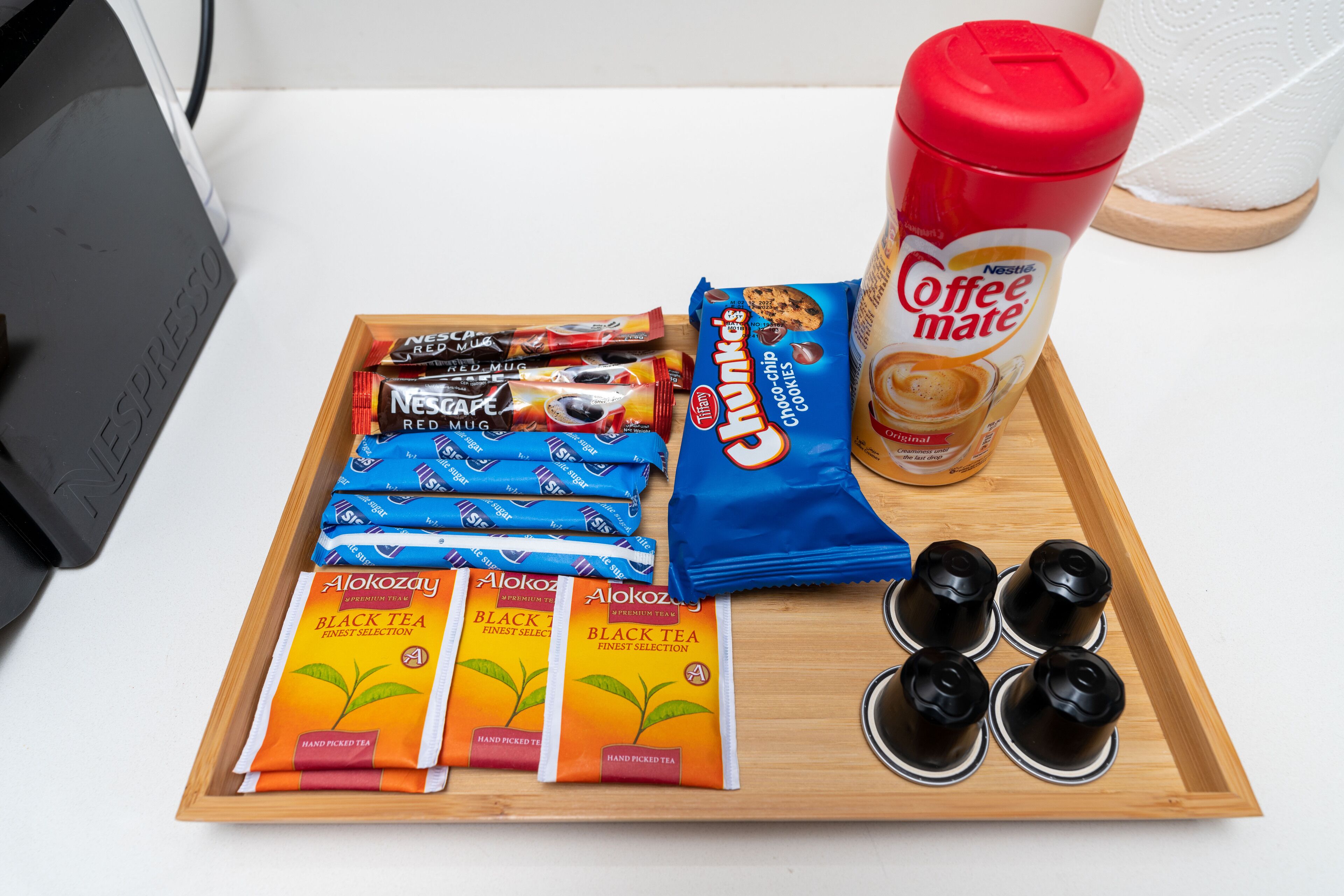 A tray with coffee and snacks, including Nestle Red Mug, Choc-chip Cookies, and Alokozay Black Tea.