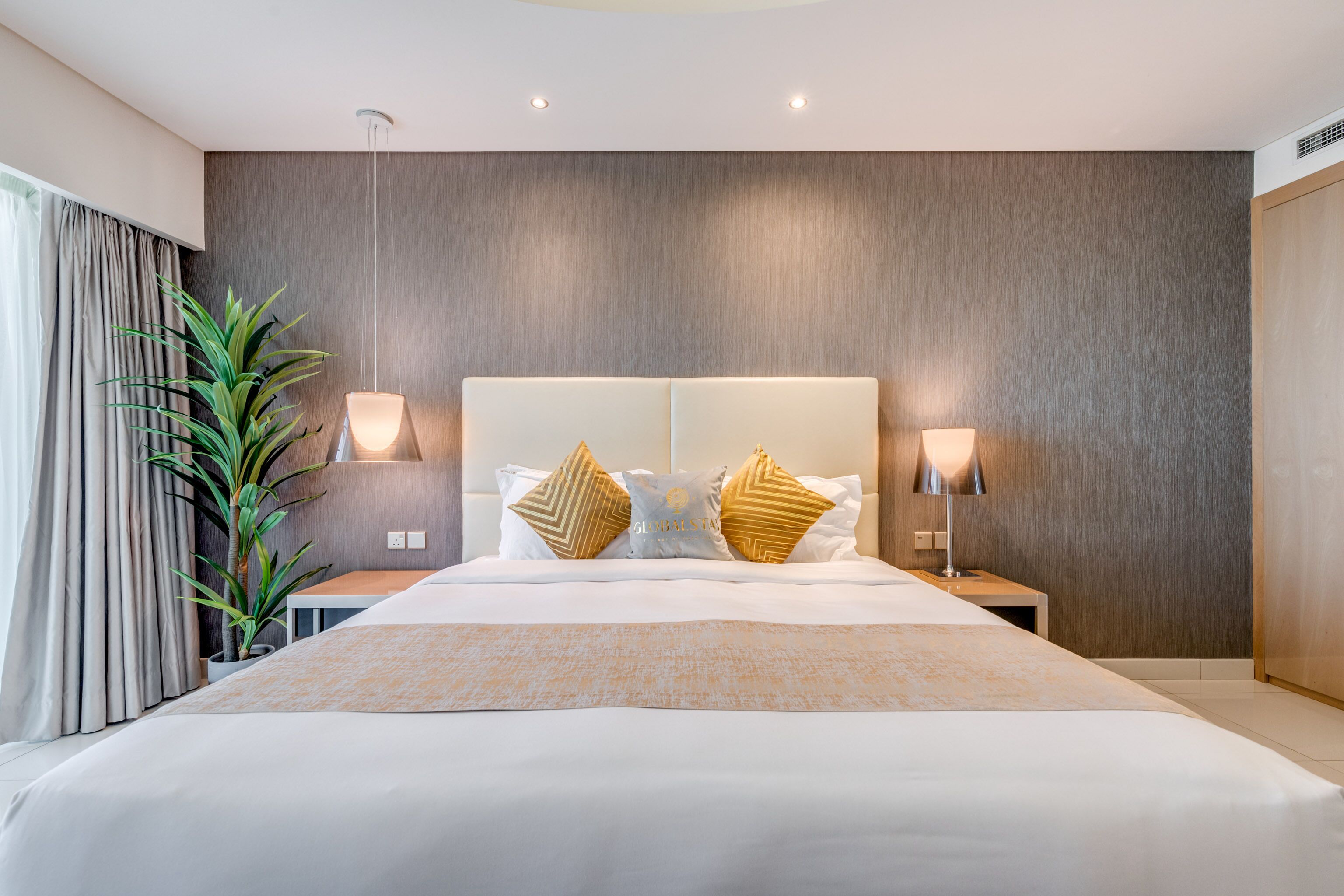 A modern hotel room with a large bed, two bedside tables, a potted plant, and a neutral color scheme.