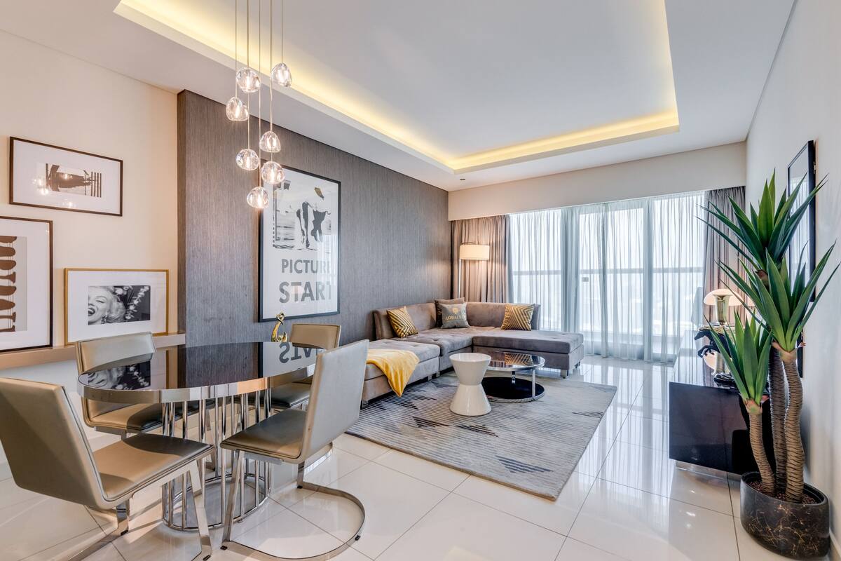 A modern living room with a sectional sofa, a dining area with a table and chairs, and a large window with curtains.