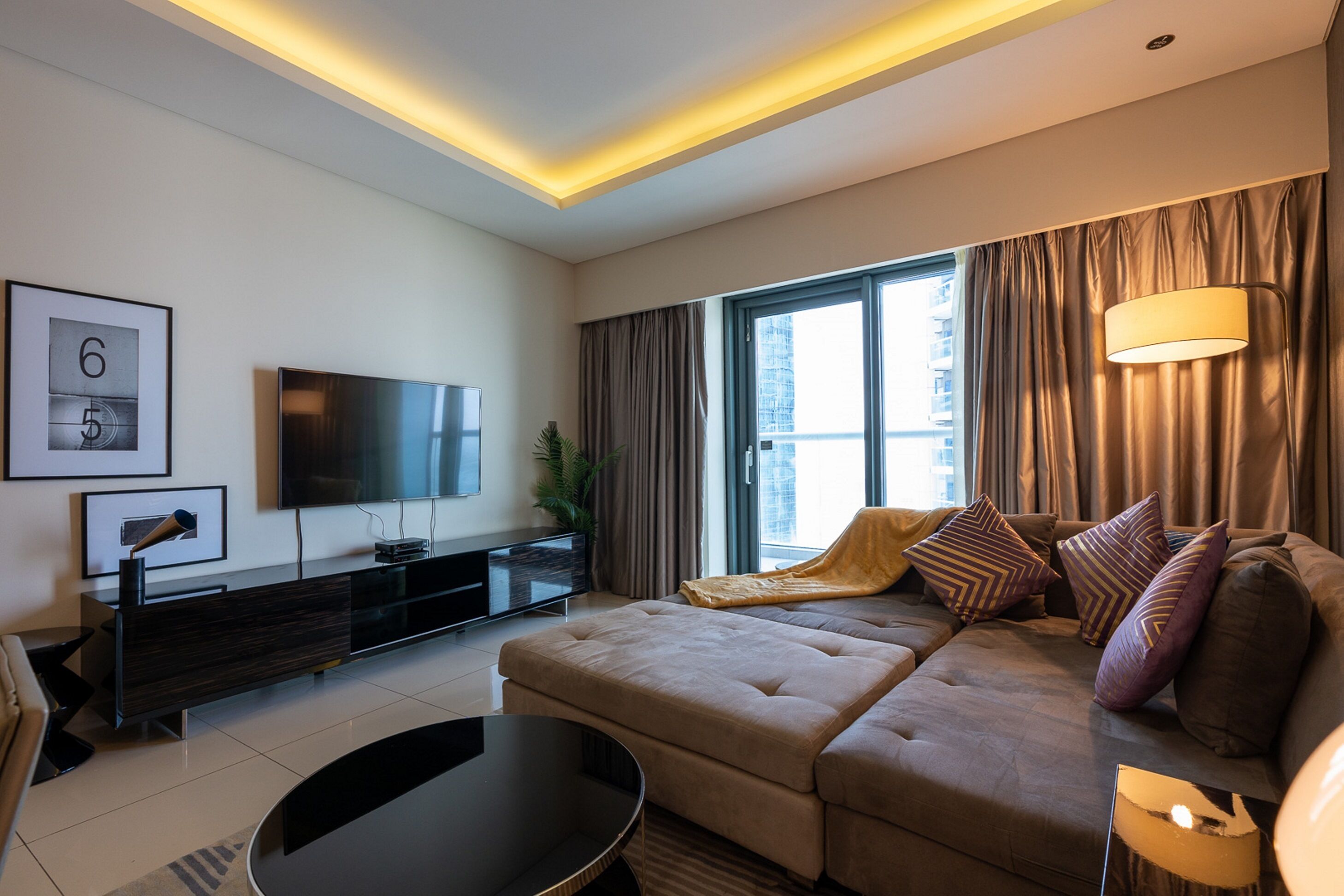 A modern living room with a sofa, a flat-screen TV, a coffee table, and a lamp.